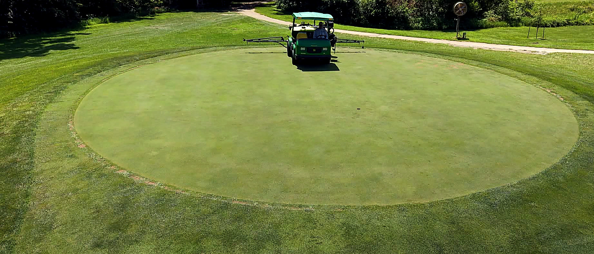 Aerial view of a golf green being sprayed, with the mown collar and surrounds around it