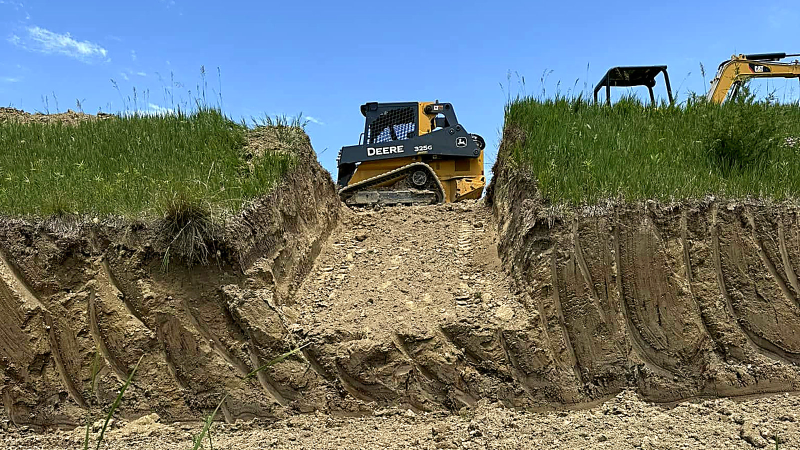 Cut bank of pale loess soil with a skid steer working the ridge above it