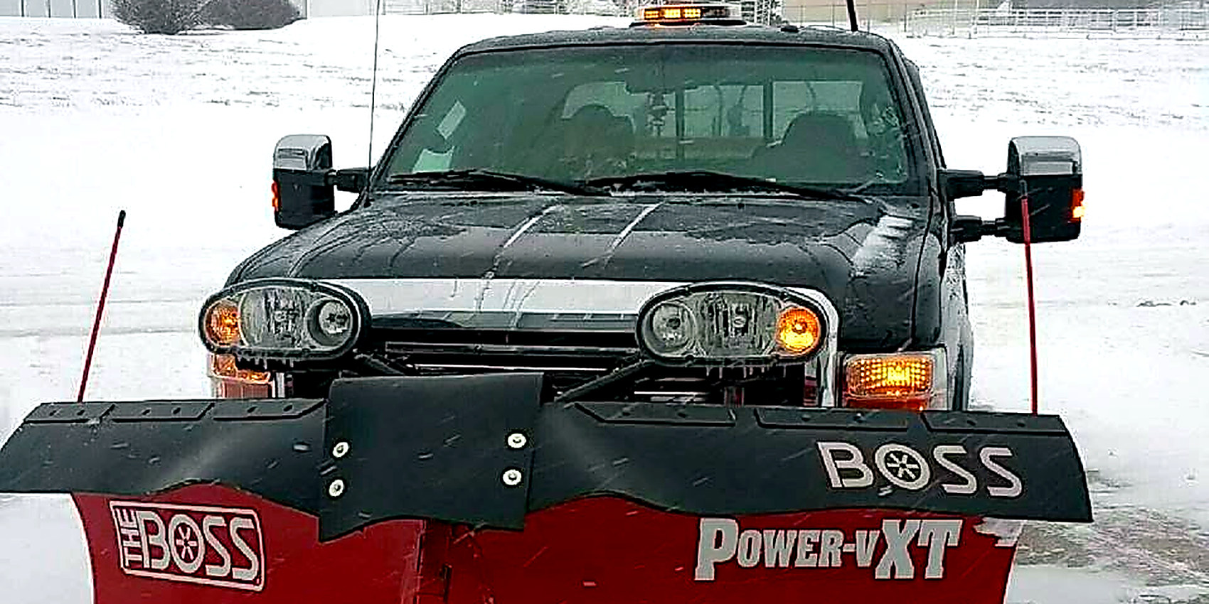 A pickup with a BOSS V-plow on a snow-covered lot, the Glenwood water tower behind it